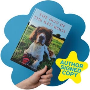 A hand holds The Dog in the Red Boot by Heather Nesbitt-Bayley, with an author signed copy badge and the book cover in view for Woofstock UK.
